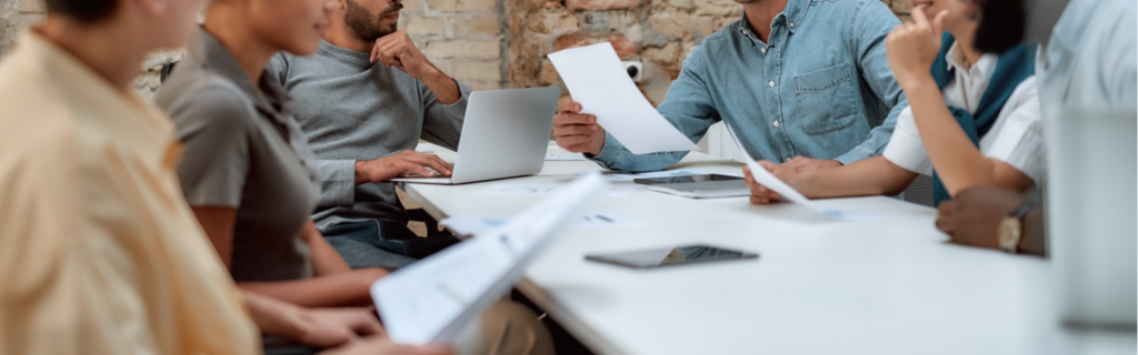 Personnes au travail , en tenue décontractée mais concentrées. Ils partagent un ordinateurs et des documents sur papier. Ambiance décontractée et sérieuse à la fois.