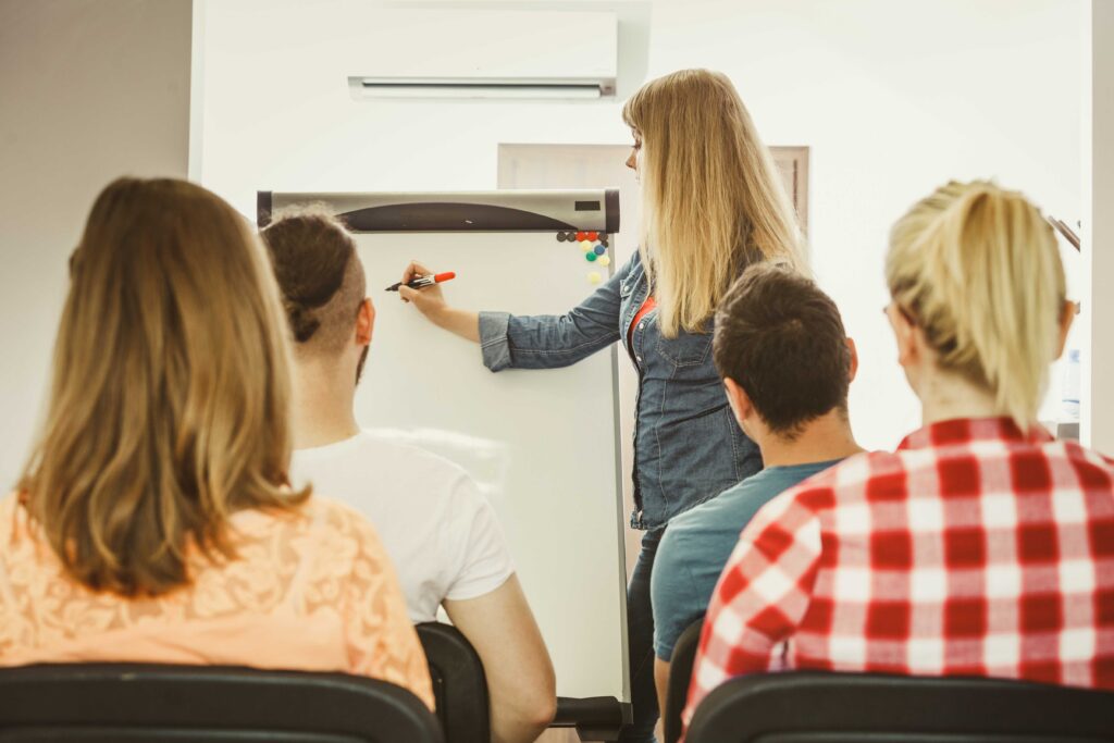 Formatrice écrivant une information sur un paperboard devant ses apprenants assis sur des chaises.
Formation d'étudiants ou de professionnels